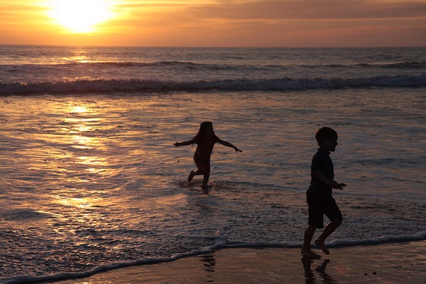 Two children play in the sea as the sun sets.